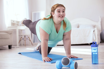 Stretching first. Plump young woman standing on all fours while doing exercises