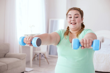 Blue weights. Plump young woman standing straight while holding dumbbells opposite her