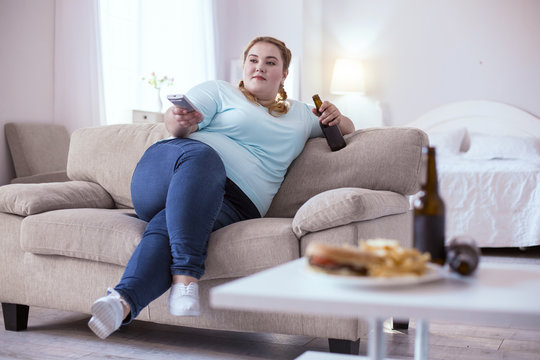Bad nutrition. Stout red-head woman drinking beer while watching television