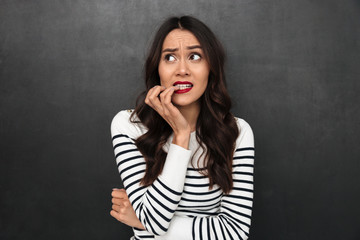 Worried pensive brunette woman in sweater bites her nails