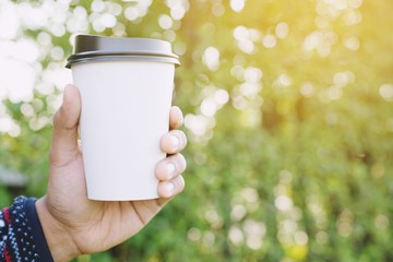 people man hand holding paper cup of take away drinking coffee on natural morning sunlight. space Place for your text or logo.