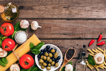 Raw ingredients for the preparation of Italian pasta, spaghetti, basil, tomatoes, olives and olive oil on wooden background. Top view. Copy space.