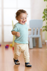 First steps of baby boy toddler learning to walk in living room. Footwear for little children.