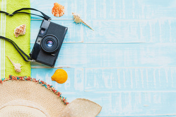 Beach accessories including sunglasses, sunscreen, hat beach, shell, green towel and retro camera on bright blue pastel wooden background for summer holiday and vacation concept.