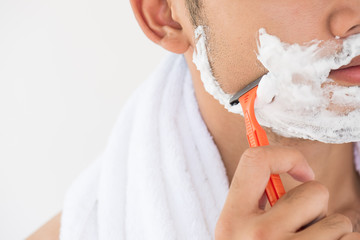 Handsome young man with foam on his face is beard shaving.