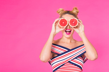 Beauty Model Girl takes Juicy Grapefruit. Beautiful Joyful young girl, funny blonde hairstyle and pink makeup.Holding Orange Slices and laughing, emotions.