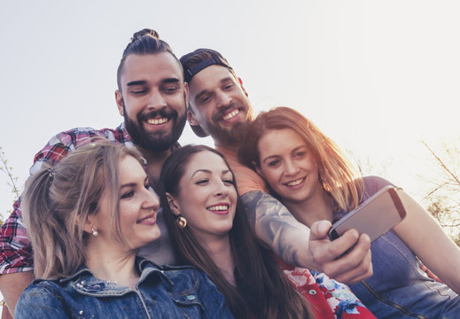 happy group of best friends millennials take a selfie photo outdoor in summer mood. sunlight from right side flaring.