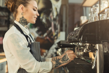 Tattooed barista making coffee in professional coffee machine - obrazy, fototapety, plakaty