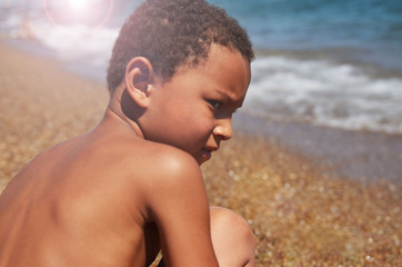 A gloomy boy sits on the beach and looks into the distance. Children who do not like salt water of the seas and oceans