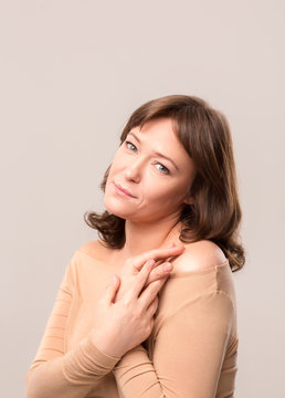 young beautiful woman in beige blouse standing half turn with crossed hands. Posing on camera. Mid age woman over 35 years old beauty concept.