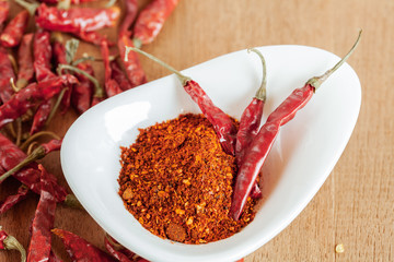 Cayenne pepper in white dish and dried chilli on wood table.