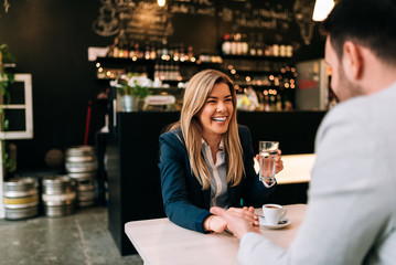 Laughing woman and man holding hands while enjoy coffee