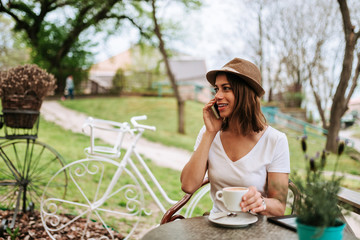 Fototapeta premium Smiling woman using her smart phone while sitting at cafe garden.