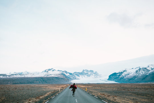 Woman Running Away To The Road On A Background Of Beautiful Mountains. Iceland Nature.