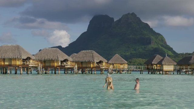 Woman splashing man in ocean near bungalows in Tahiti / Bora Bora, French Polynesia