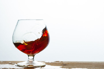 Glass of brandy or cognac splash on the wooden and white background with copy space