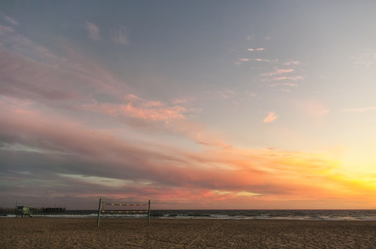 A beautiful pink and orange sunset over a sandy beach in Los Angeles, California, USA. Twilight on a Californian beach with a volleyball net and a typical lifeguard tower in the background