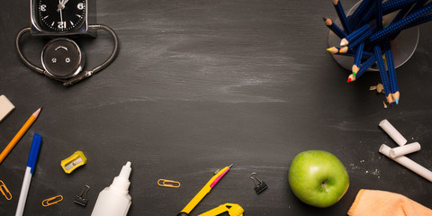 school supplies, alarm clock, pencils, apple on black chalkboard top view, copy space. concept: back to school background, school's out, school holidays. long banner