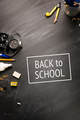 school supplies, alarm clock, pencils on black chalkboard top view, copy space, vertical framing. text back to school . blackboard background