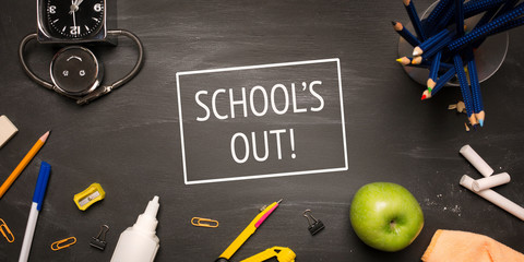 school supplies, alarm, pencils, apple on black chalkboard top view, inscription school's out, school holidays. long banner