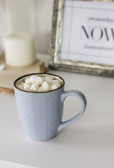 Blue mug with cocoa, coffee, marshmallows on white table with decor