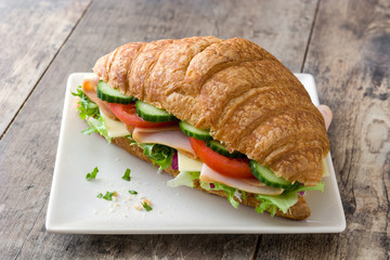 Croissant sandwich with cheese, ham and vegetables on wooden table