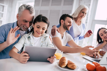 The happy family sitting with a laptop and the tablet at the table