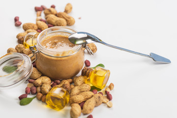 Natural peanut butter with oil in a glass jar and peanuts