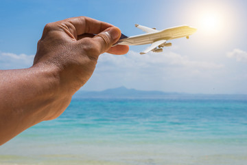 Hand holding a plane with beautiful beach and sea in background. Go to holidays by airplane