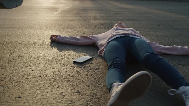 Girl laying in street with cell phone near car bumper after accident / Cedar Hills, Utah, United States