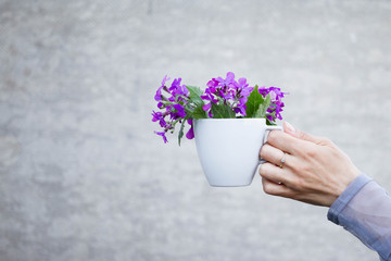 A woman holds a white cup with small purple flowers