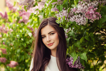 Pretty brunette woman with long healthy hair and natural makeup on floral background outdoors