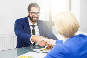 Business colleagues, bearded man and blonde woman, have work contract agreement sitting in white office room, handshake deal concept