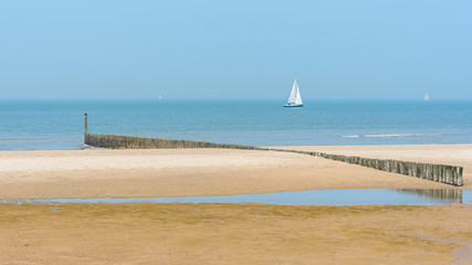 Breakwater on a beach of Holland, sailboats in background
