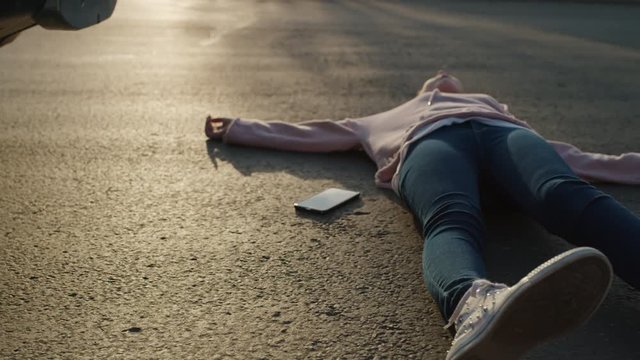 Girl laying in street with cell phone near car bumper after accident / Cedar Hills, Utah, United States
