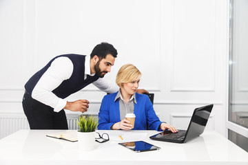 Two business colleagues work with laptop holding cups of coffee in white office interior