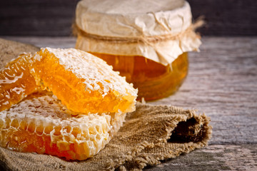 Honey background. Sweet honey in the comb, glass jar. On wooden background.