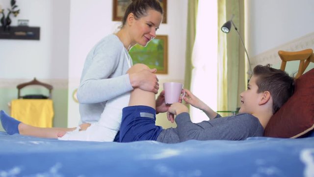 Mother brings a cup of tea to her son with broken leg, maternal care