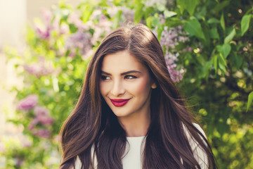 Fototapeta premium Spring woman outdoor. Cheerful smiling female model girl with healthy brunette hair in blossom park outdoors, cute face closeup
