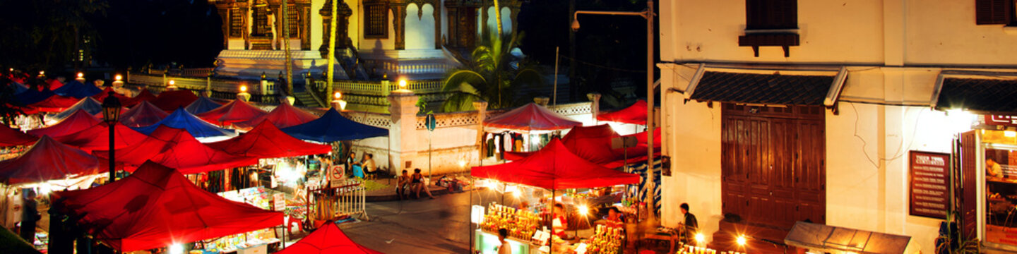 Famous Night Market In Luang Prabang, Laos With Illuminated Temple