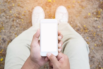 close up of hand holding white mobile phone with blank white screen on thigh with white canvas shoes sitting on garden , feeling relaxed,top view