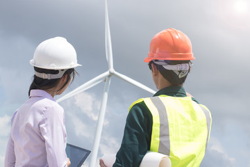 Two male and female engineers are working at the wind turbine.