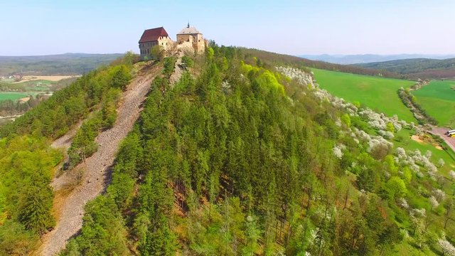 Drone flight around Tocnik Castle in blooming orchard. A royal chateau of Wenceslas IV from the 14th century, adjusted in the Renaissance and the Baroque styles. Famous Czech monument from above. 