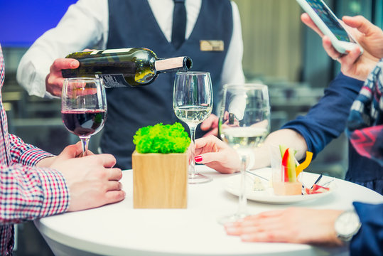 Professional waiter in uniform serving wine to guests of event. Catering or celebration concept. Service at business, corporate meeting, party, weddings. Selective focus, space for text.