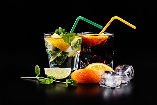Mojito and rum and cola alochol cocktail served in highball glasses with lemon, orange, mint and ice stand on black background