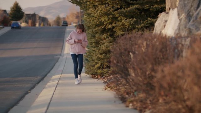 Oblivious girl walking on neighborhood sidewalk texting on cell phone / Cedar Hills, Utah, United States