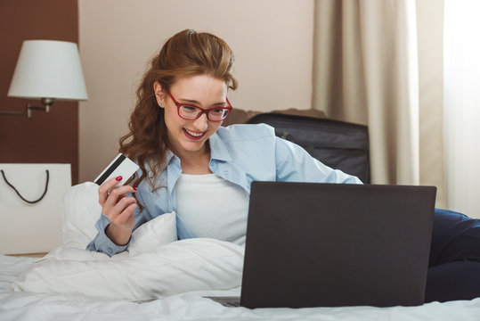 Happy businesswoman shopping online with credit card and laptop, sitting on bed, making order with mobile phone, copy space