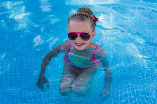 A cute little funny girl in sunglasses on vacation at the pool