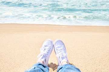 Fototapeta na wymiar Female feet in jeans and white sneakers on beach. Walk along the beach