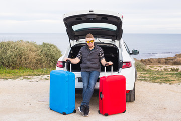 Guy standing in back of car smiling and getting ready to go. Young laughing man standing near open trunk of a car. Summer road trip